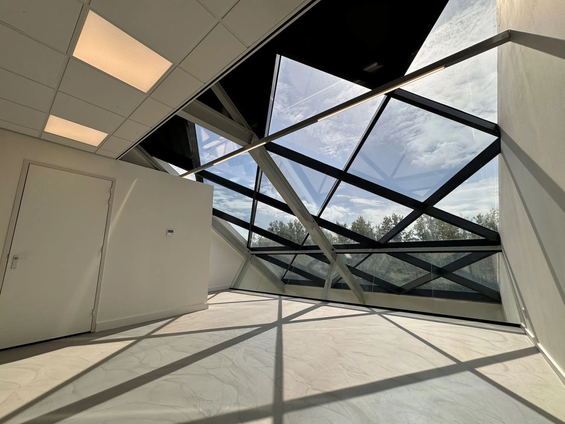 Lichte, moderne ruimte in Mart Stamhof met een schuine glazen gevel en zicht op bomen.